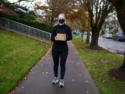Woman wearing mask delivering a package on a fall day in a suburban area.
