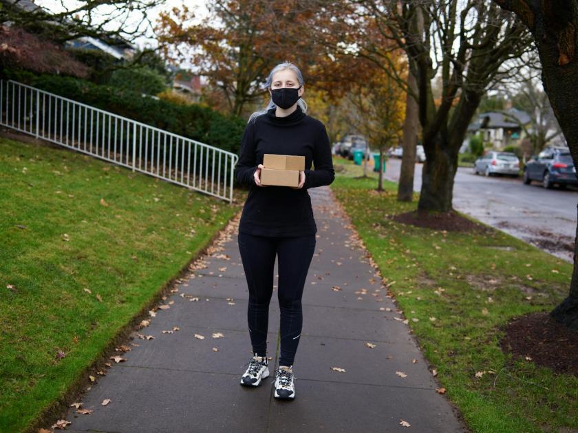 Woman wearing mask delivering a package on a fall day in a suburban area.