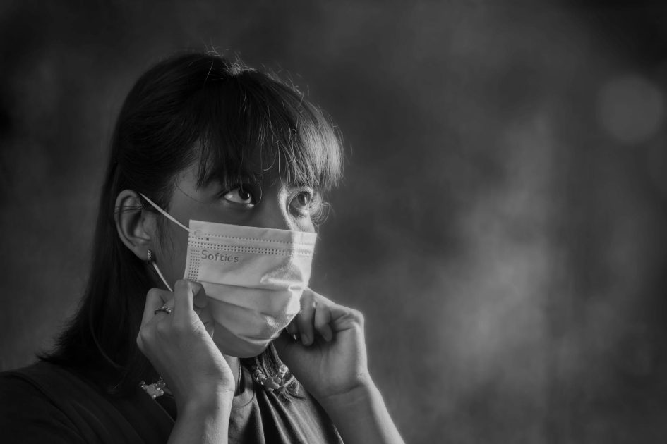 Masker Medis 3 Ply: Panduan Lengkap Memilih & 7 Tips Penggunaan 1 Black and white portrait of a woman adjusting her face mask, conveying protection and awareness.