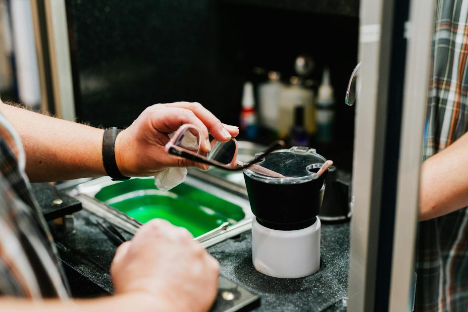 Ultrasonic Cleaner Laboratorium: Panduan Lengkap + 7 Tips Memilih 1 Close-up photo of a person cleaning eyeglasses in a workshop setting, focused on hands and tools.
