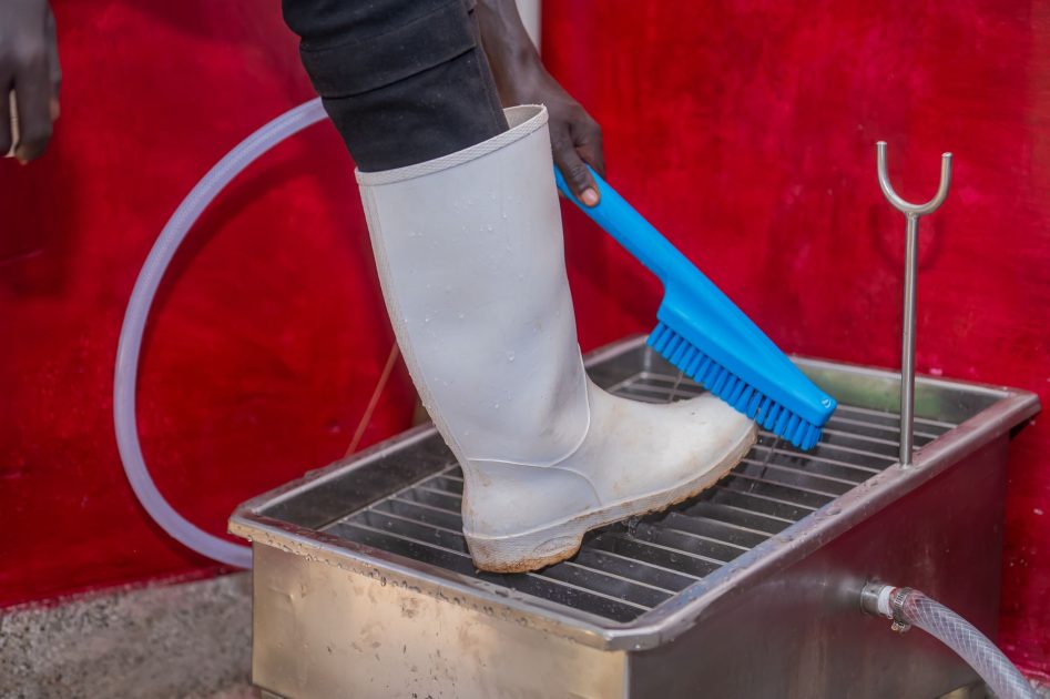 7 Kegunaan ABS Clamshell Wall Hanging Eye Washer 1 Person scrubbing boots with brush in a stainless steel wash basin in Eldoret, Kenya