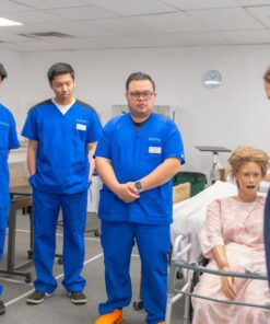 Nursing students in blue scrubs practicing patient care using a medical mannequin.