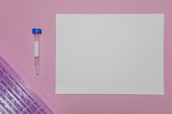 Simple setup with a blank paper and test tube on a pink background for lab mockups.