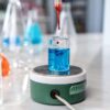 A laboratory experiment with a dropper adding red liquid to blue solution in glassware on a magnetic stirrer.