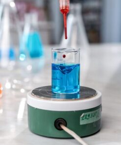 A laboratory experiment with a dropper adding red liquid to blue solution in glassware on a magnetic stirrer.