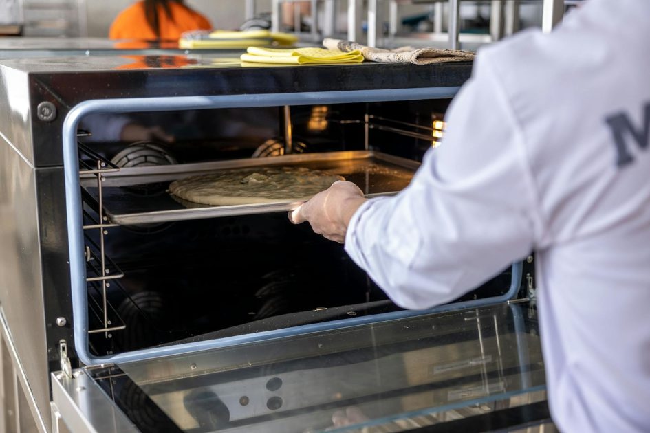 Cara Menggunakan Glass Baking Oven: Panduan Lengkap 2024 1 Chef places uncooked pizza into an industrial oven in a professional kitchen setting.