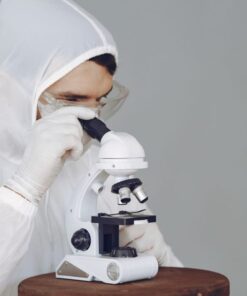 Scientist in protective gear using a microscope, focused on research and analysis.