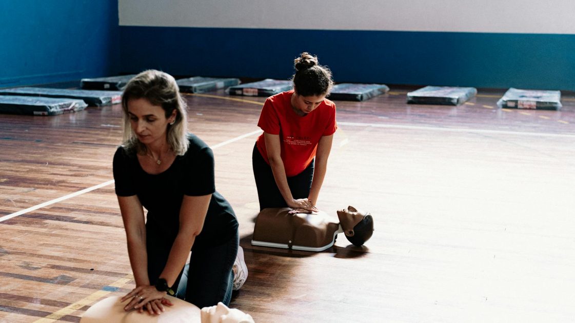 LAERDAL TeamReporter aplikasi pelatihan CPR - Aleson Padilha Two women learn CPR techniques on mannequins during a first aid training session.