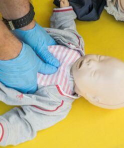 Hands performing CPR on an infant mannequin for a first aid training session.
