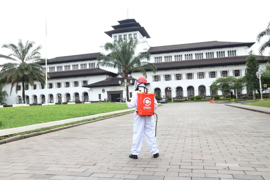Alasan Prabowo Copot Dadan Kepala BGN: 7 Fakta Penting 1 A person in protective clothing disinfects an area in front of a historic building with palm trees.