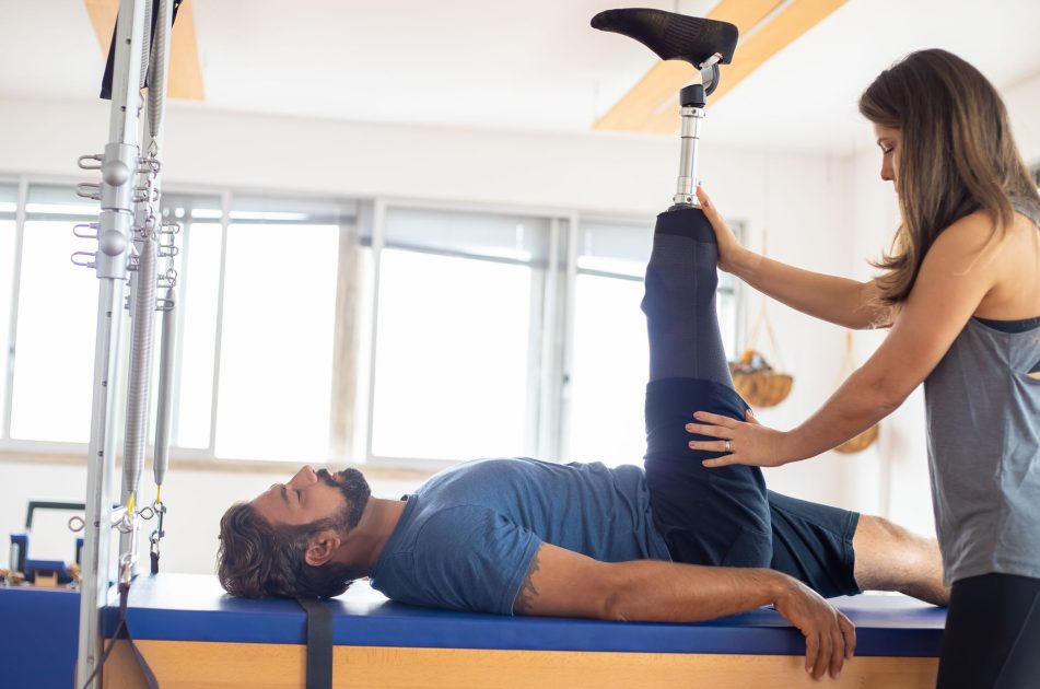 7 Alat Fisioterapi Rumah Terbaik 2025: Panduan Lengkap 1 Personal trainer assists amputee in rehabilitation exercise indoors.
