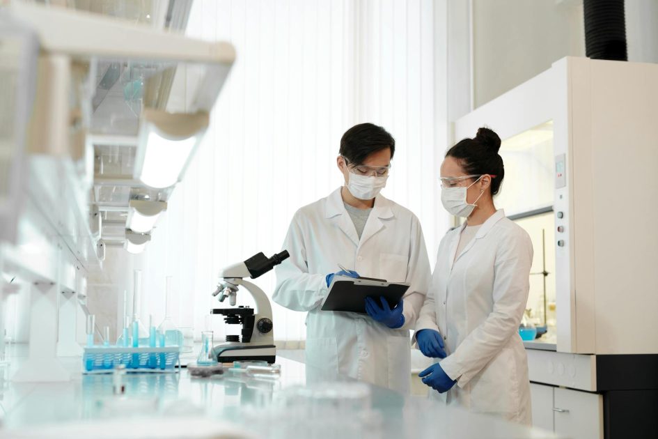 Alat Fume Hood: 7 Fungsi Penting & Panduan Lengkap 2024 1 Two scientists in a laboratory wearing masks, discussing research with a microscope.