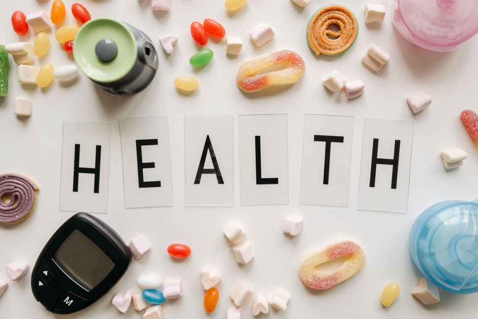 Ancaman Gula Berlebih Balik Manfaat: 7 Fakta Penting 2024 1 Creative flat lay with sweets around a 'HEALTH' text and monitoring device, symbolizing diabetes awareness.