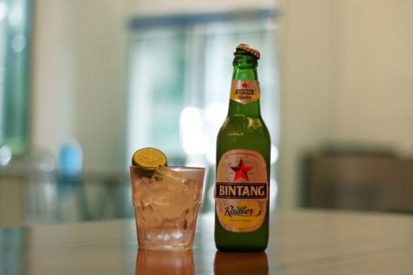 Bintang Radler beer bottle and iced lemon drink on a reflective surface indoors.