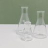 A set of three clear glass laboratory flasks on a clean white and green background, ideal for science themes.