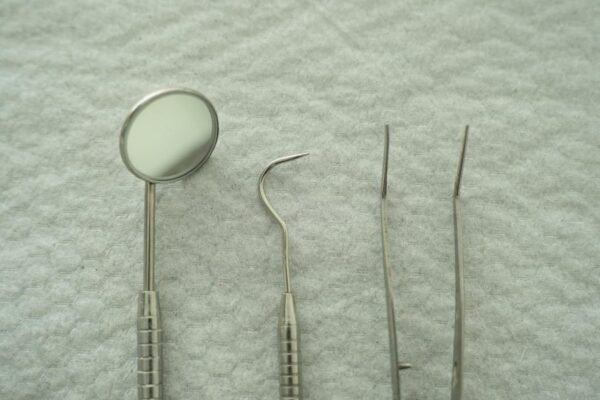 Close-up of dental tools including mirror and pick on a gray textured background.