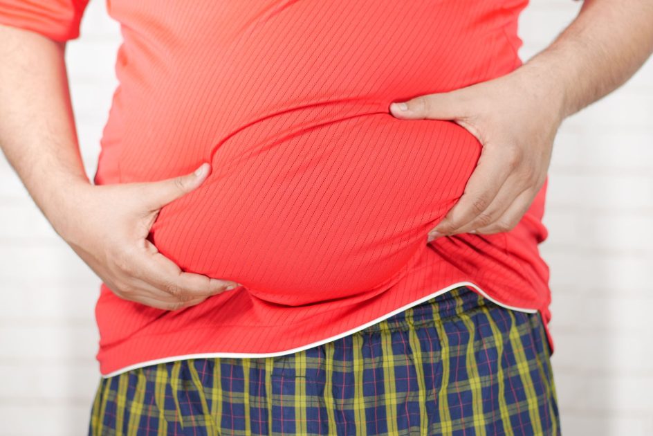 Diremehkan Obesitas Sentral Memicu Perlemakan: 7 Fakta Kritis 1 Close-up image of a man holding his bloated belly while wearing a red shirt.