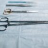 Close-up of surgical tools including a needle holder on a blue cloth in a medical setting.