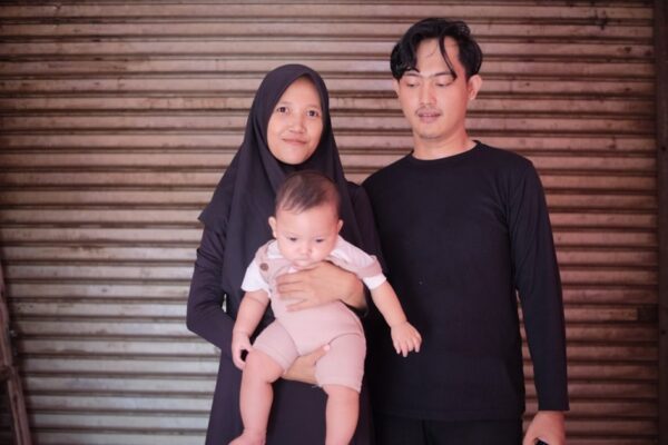 a man and a woman standing next to each other holding a baby