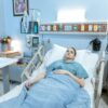A young woman lies in a hospital bed during her recovery process in a calm, well-equipped room.