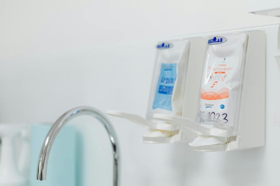 Close-up of wall-mounted dispensers for hand sanitizers next to a hygienic sink faucet.