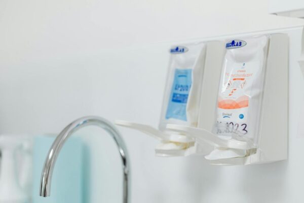 Close-up of wall-mounted dispensers for hand sanitizers next to a hygienic sink faucet.