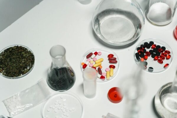 Variety of pills, herbs, and chemical glassware on a white table.