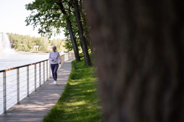A senior woman enjoys a healthy walk on a lakeside boardwalk on a sunny day.