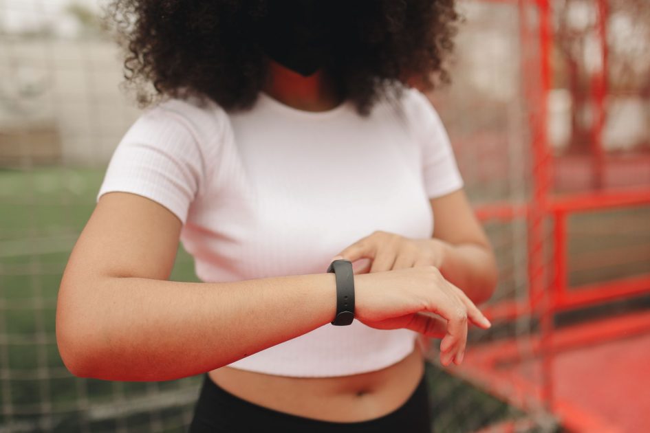 Young woman wearing a fitness tracker, checking time in an outdoor sports area.