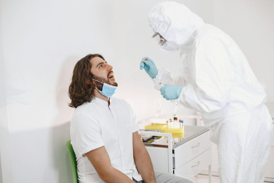 Healthcare worker in protective gear swabbing a man for COVID-19 indoors.