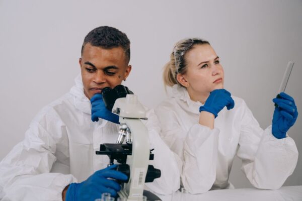 Two scientists in lab coats conduct research with microscope and test tube.