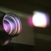 Close-up view of a projector lens with light reflections, highlighting optics and technology.