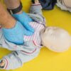 Manekin Resusitasi Bayi Laerdal NeoNatalie | Pelatihan CPR 1 Hands performing CPR on an infant mannequin for a first aid training session.