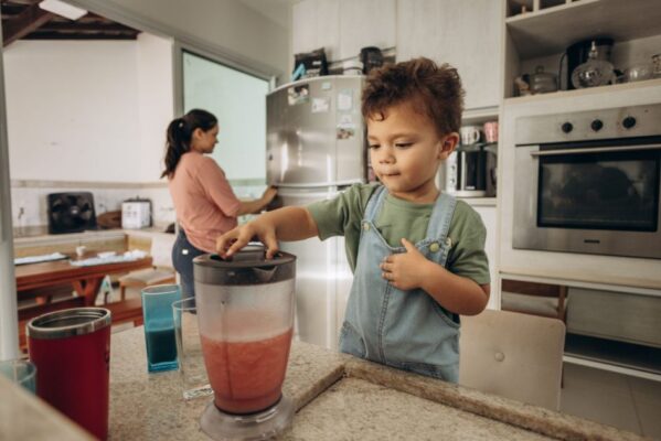A young boy helps his mother make a smoothie using a blender in a modern kitchen.