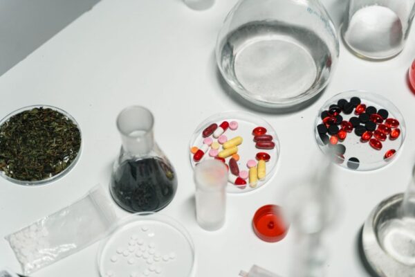 Variety of pills, herbs, and chemical glassware on a white table.