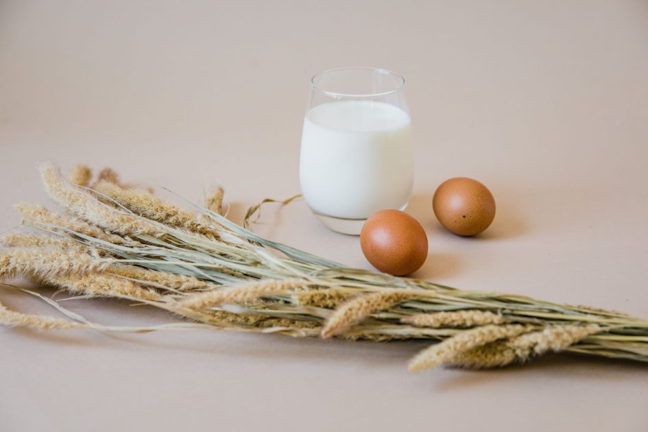 Minuman Multigrain Hotto Gandeng Indro: 7 Panduan Lengkap Hidup Sehat 1 Still life of a glass of milk, brown eggs, and wheat stalks on a beige background.