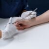 Medical professional suturing an injury on a person's arm with surgical instruments.