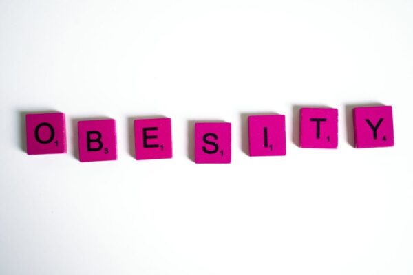 Purple Scrabble tiles spelling 'obesity' on a white surface, conceptual still life.