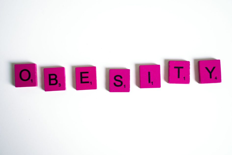Purple Scrabble tiles spelling 'obesity' on a white surface, conceptual still life.