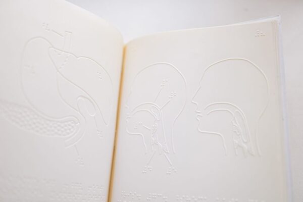Detailed close-up of embossed anatomy diagrams on an open braille book page.