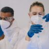 Two laboratory scientists in protective gear conducting experiments with test tubes.