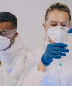 Two laboratory scientists in protective gear conducting experiments with test tubes.