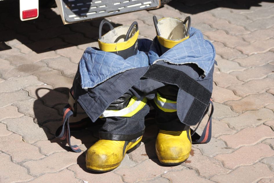 Close-up of firefighter turnout gear with yellow boots on paved ground, symbolizing readiness.