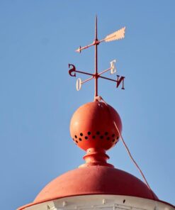 A weather vane atop a red dome under a clear blue sky, symbolizing direction and weather changes.