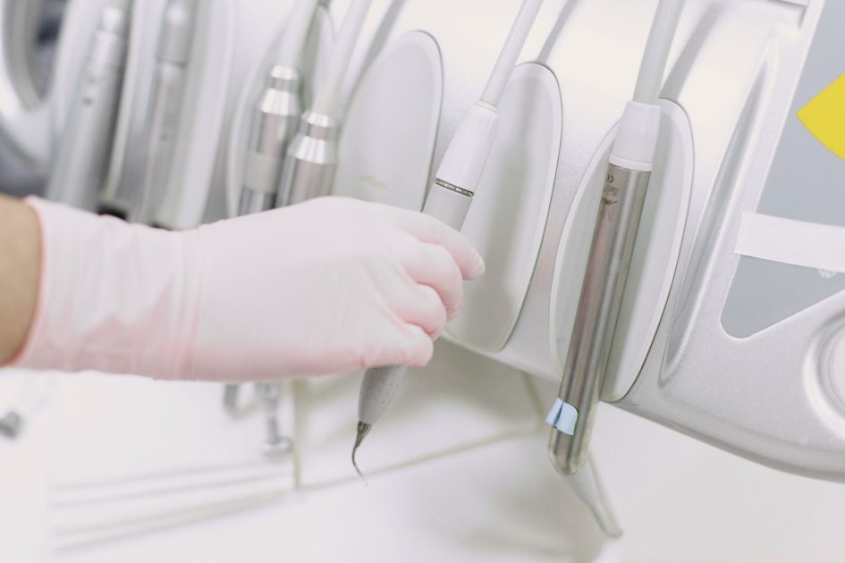 Perbedaan Tukang Gigi & Dokter Gigi: 7 Fakta Penting 1 Close-up of a gloved hand operating dental tools in a sterile clinic environment.