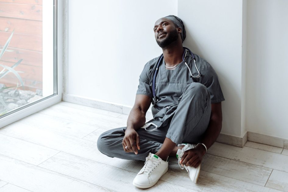 Piala Dunia 2026 Dihantui Suhu Panas: 7 Panduan Kesehatan 1 A tired healthcare professional in gray scrubs resting against a wall, reflecting exhaustion.