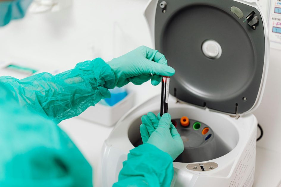 Lab technician operates a centrifuge machine, handling tubes with gloves.