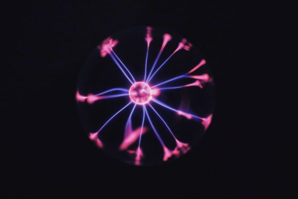 Transparent glass plasma ball with bright neon luminous against dark background in room