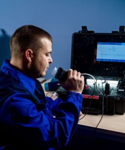 A technician in blue uniform using portable diagnostic equipment indoors.