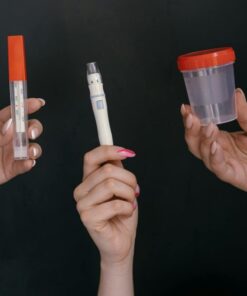 Three hands holding medical tools including a thermometer, lancet, and specimen container.